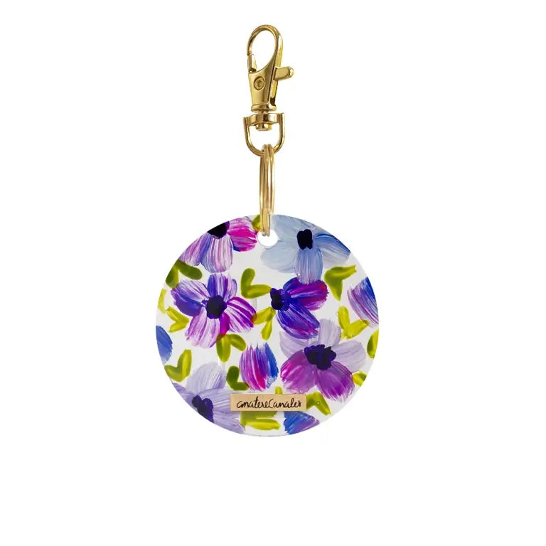 Llavero circular pintado a mano por Ana Tere Canales. Un diseño de flores en morados y verdes.